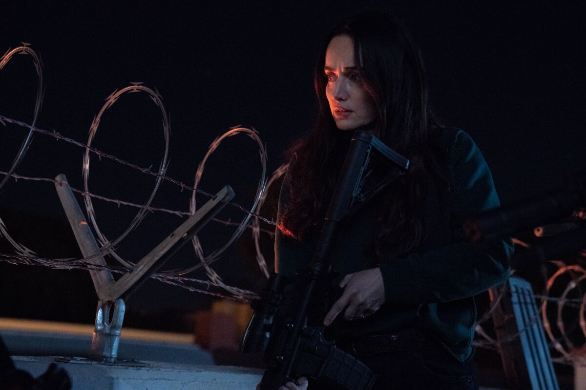 A young woman sits on a wall topped with barbed wire.