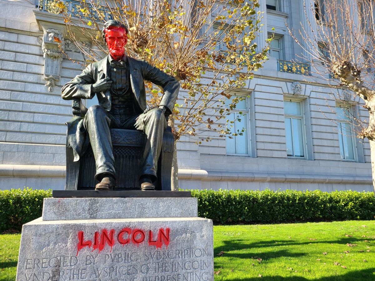 Red spray paint covers the face of a statue of Lincoln and outlines his name.