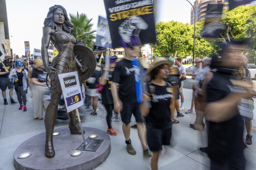 BURBANK, CA - AUGUST 01: Picketers walk past a Wonder Woman statue at Warner Bros. Studio in Burbank on Thursday, Aug. 1, 2024. Video game actors, with many SAG-AFTRA supporters, walked the picket line. (Myung J. Chun / Los Angeles Times)