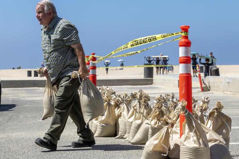 Seal Beach, CA - August 18: John Straub, left, a volunteer with West Orange County Community Emergency Response Team (CERT) loads dozens of sandbags for local residents to fortify their homes as surfers with the M&M Surf School head in ahead of anticipated high surf, strong winds and flooding from the approaching Hurricane Hilary in Seal Beach Friday, Aug. 18, 2023. As Hurricane Hilary continues its march toward Southern California, officials have issued an unprecedented tropical storm watch for the region. The watch is in effect for much of southwestern California, from the San Diego deserts to the San Bernardino County mountains and onto Catalina Island, something the National Hurricane Center said is a first for this area. A tropical storm watch indicates that tropical storm conditions are possible - meaning more than 39 mph sustained winds - within 48 hours, according to the hurricane center. (Allen J. Schaben / Los Angeles Times)