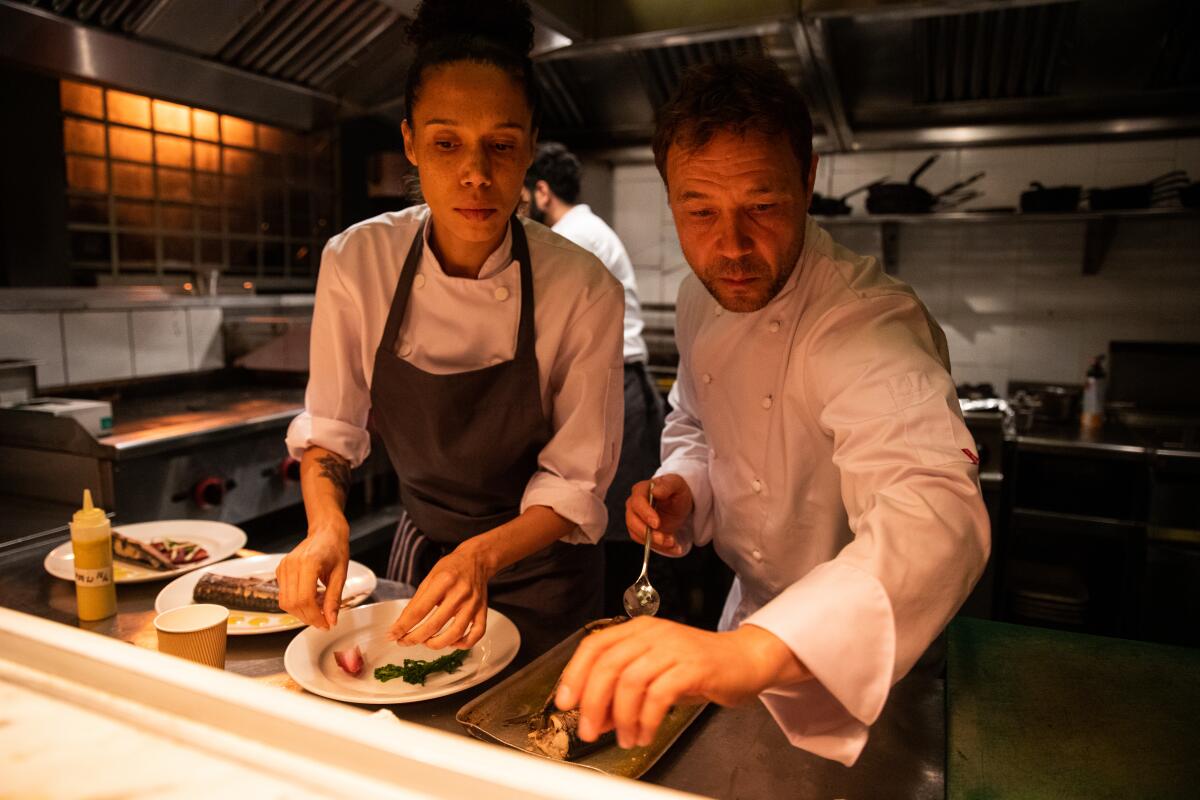 Two chefs stand side by side plating food in a restaurant kitchen.