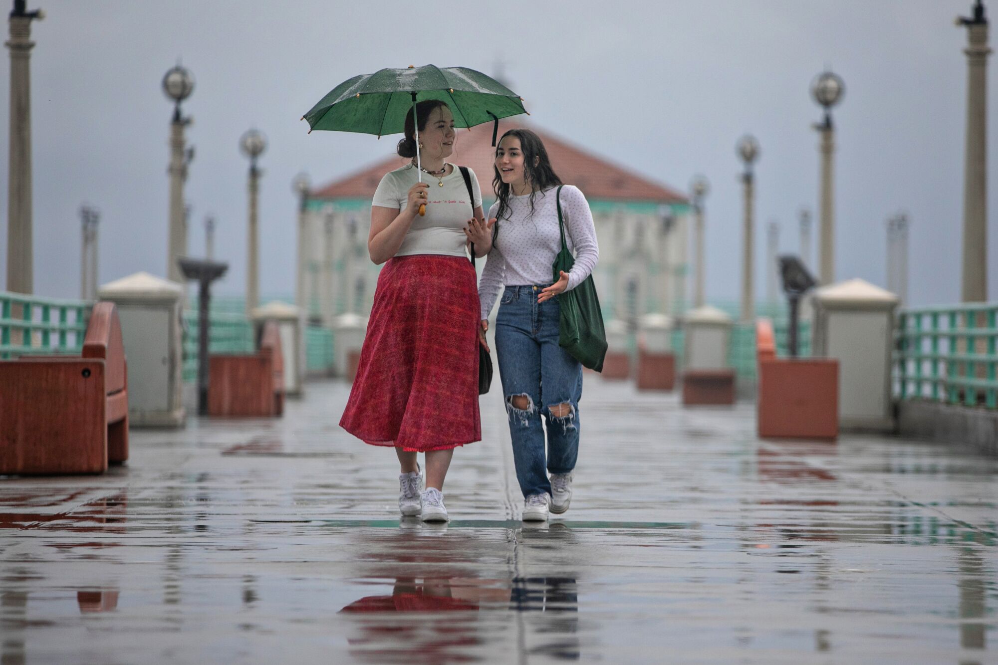 Two women walk on a pier in the rain.