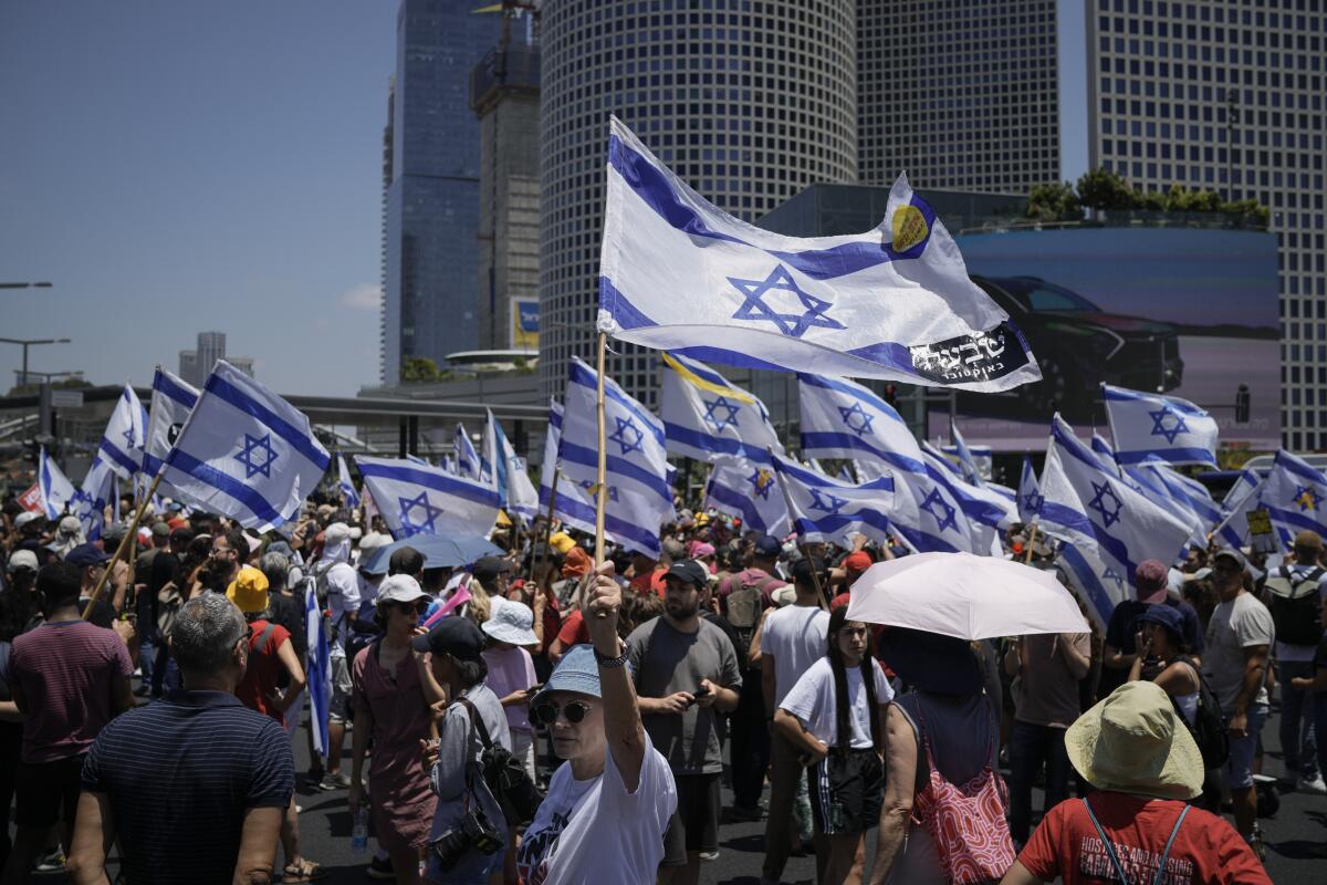 Demonstrators wave Israeli flags during a protest near buildings.