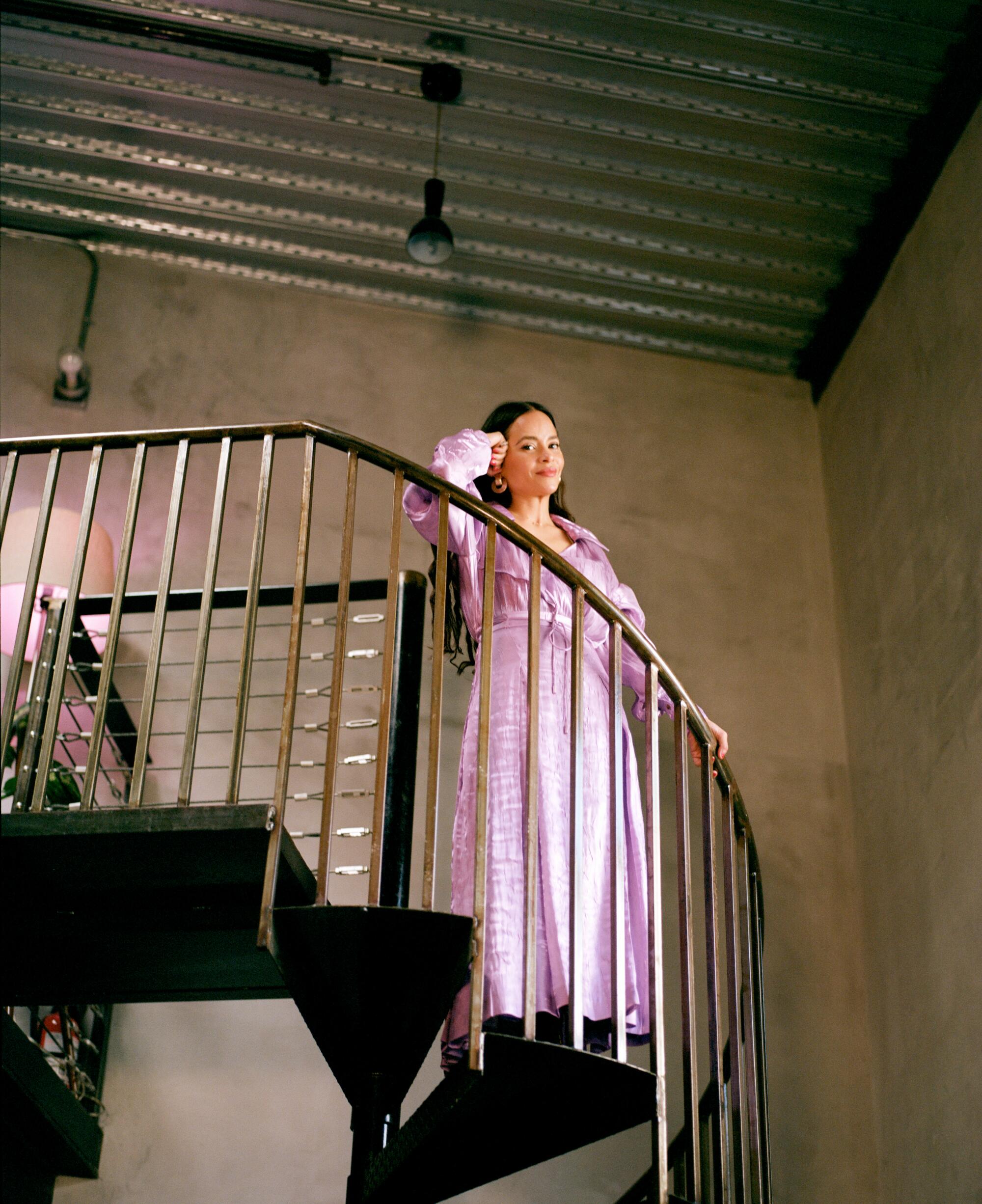 A woman in a pink dress stands at the top of a spiral staircase.