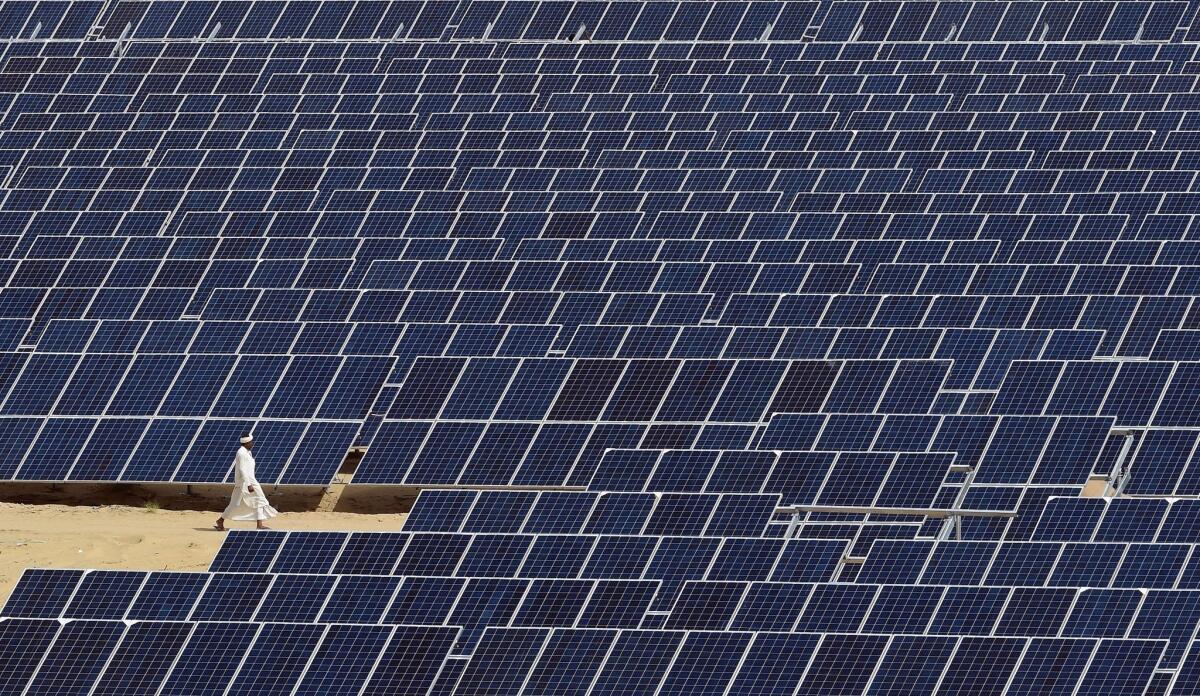 A worker walks past solar panels at the Roha Dyechem power plant at Bhadla, India, on Aug. 23.