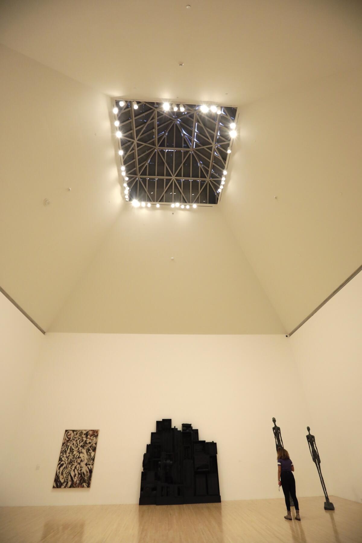 A gallery with very tall ceilings contains a skylight that has been covered up and replaced by artificial illumination.