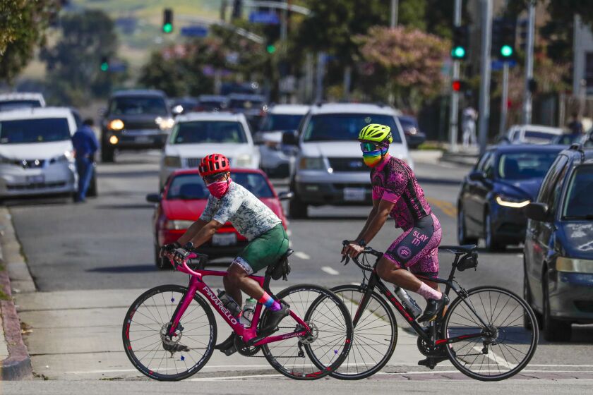LOS ANGELES, CA - APRIL 11: Two cyclists wearing face masks paddle down Cesar E. Chavez Blvd on Saturday morning in Los Angeles. Life around Cesar E. Chavez Blvd. and Soto St. has slow down as California officials extended stay-at-home orders into May and residents entered Easter weekend with unprecedented limits on their movements. Most of the people are adhering to the orders by mayor to wear masks while out running errands. Los Angeles, CA. (Irfan Khan / Los Angeles Times)