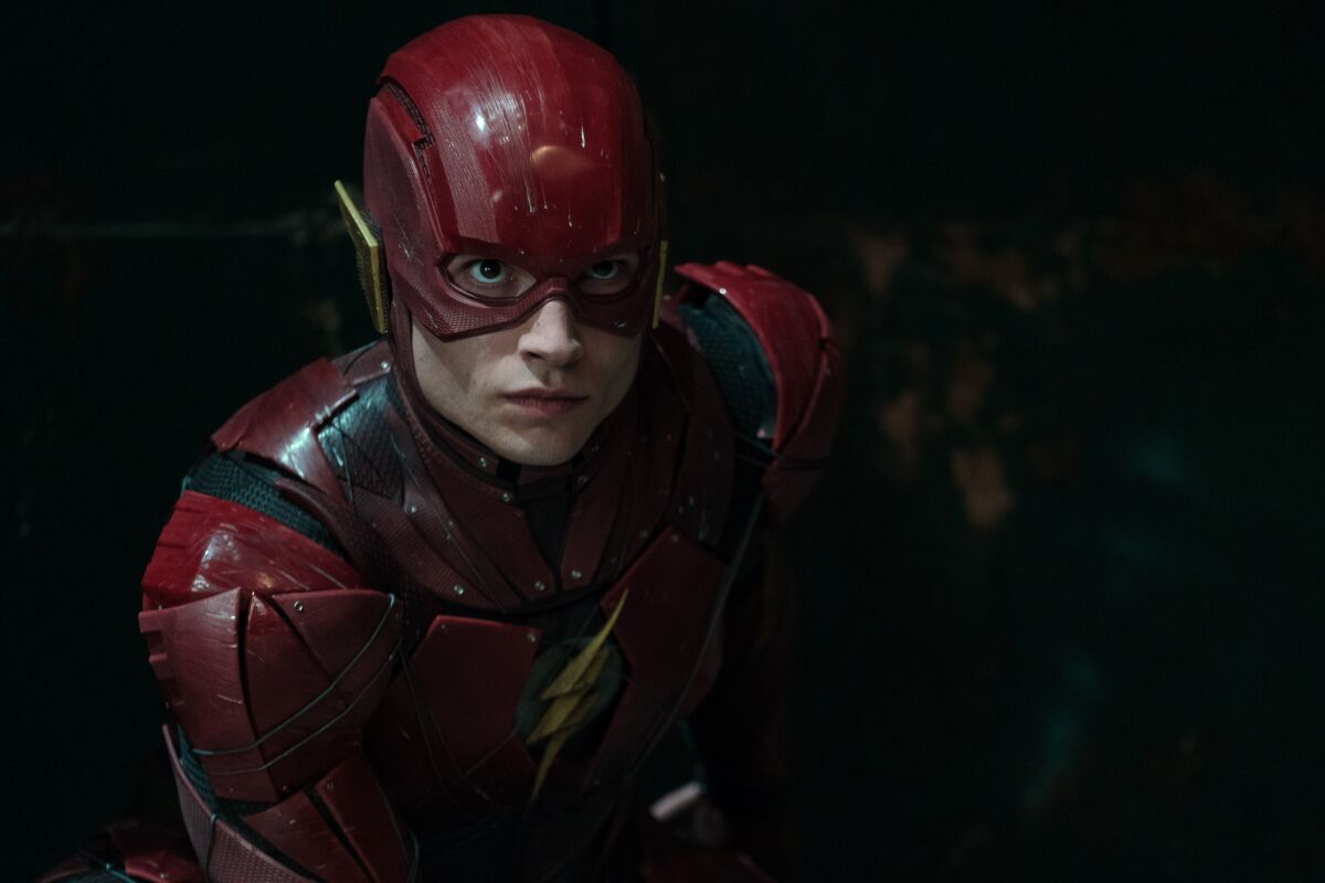 A person in a red superhero outfit with gold accents stares ahead intently.