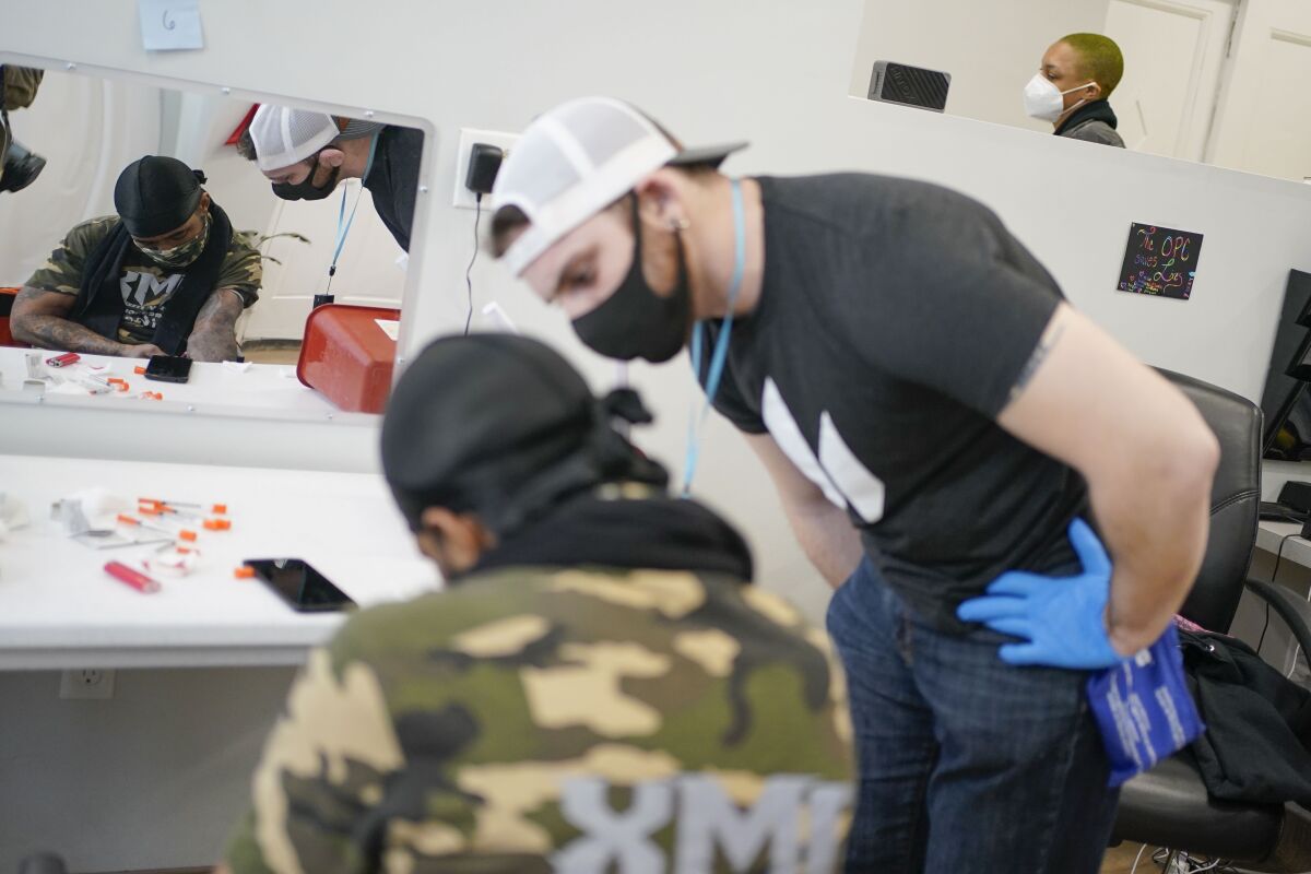 Brian Hackel, right, an overdose prevention specialist, helps Steven Baez, a client suffering addiction, find a vein to inject intravenous drugs at an overdose prevention center, at OnPoint NYC in New York, N.Y., Friday, Feb. 18, 2022. Also known as a safe injection site, the privately run center is equipped and staffed to reverse overdoses, a bold and controversial contested response to confront opioid overdose deaths nationwide. (AP Photo/Seth Wenig)