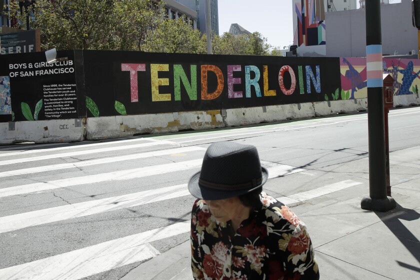 A person walks across the street from a sign for the Tenderloin neighborhood in San Francisco, on Aug. 21, 2019. 