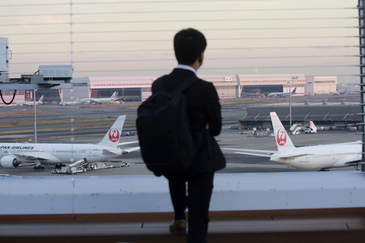 A man looks at Japan Airlines planes parked at Haneda international Airport in Tokyo, on Nov. 29, 2021. NHK TV said Wednesday, Dec. 1, that Japan will suspend new reservations on all incoming flights for a month to guard against new virus variant. (AP Photo/Koji Sasahara)