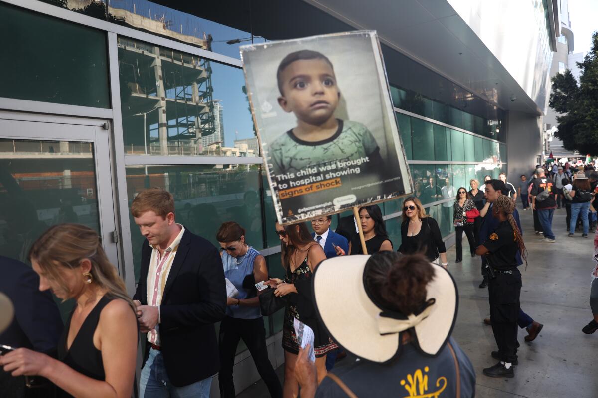 A protester holds a photo of a Palestinian boy before a crowd of people on a downtown L.A. sidewalk near the Peacock Theater