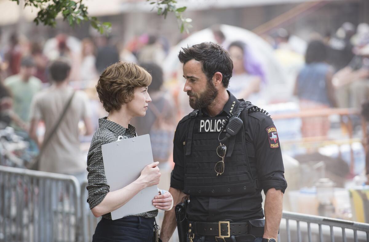 A woman holding a clipboard and a man in a police uniform standing in front of a low crowd barrier.