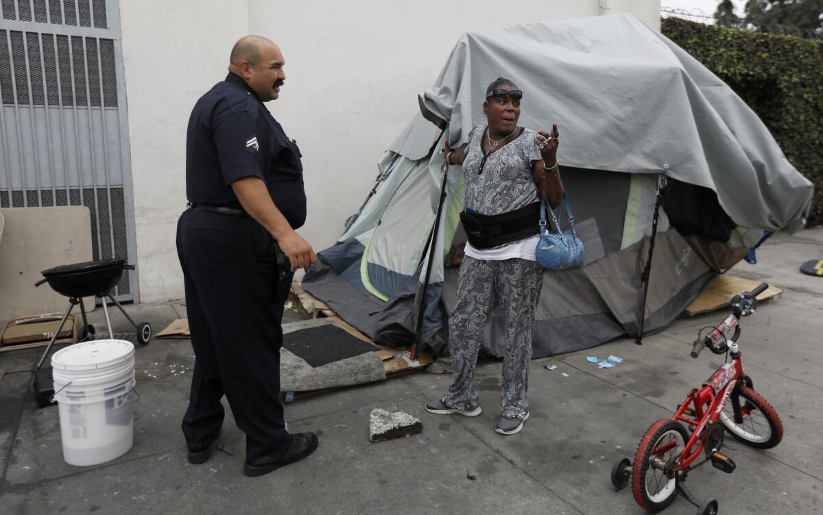 Police Officer Jerry Ballesteros, left, speaks with Big Mama outside her tent before a sanitation cleanup on Broadway Place.