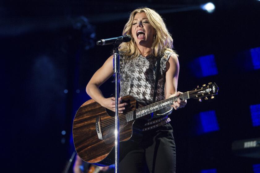 Kimberly Perry of The Band Perry on stage wearing a sleeveless shirt and holding a guitar 