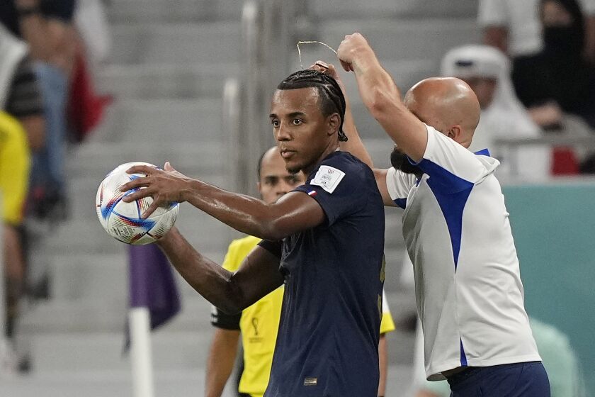 An assistant coach takes of the necklace of France's Jules Kounde during the World Cup round of 16 soccer match between France and Poland, at the Al Thumama Stadium in Doha, Qatar, Sunday, Dec. 4, 2022. (AP Photo/Martin Meissner)