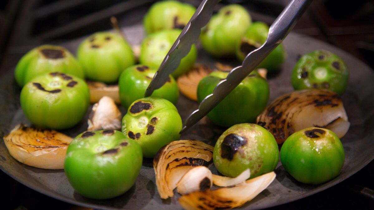 A comal, or griddle, is used to prepare roasted tomatillos and onions for a smoked tomatillo salsa.