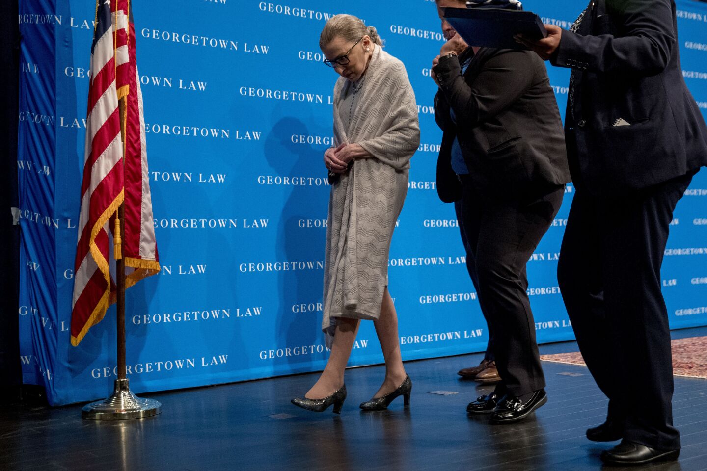 Justice Ruth Bader Ginsburg walks in front of a blue background with the words "Georgetown Law"