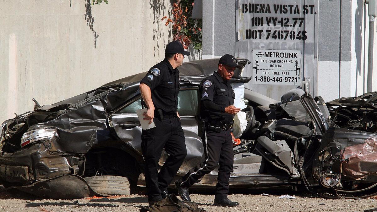Police officers walk by a mangled vehicle that was clipped by a Metrolink train near near the intersection of San Fernando Boulevard and Buena Vista Street. (Tim Berger / Burbank Leader)