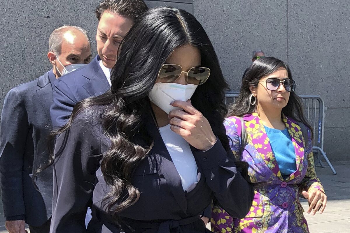 A woman with long black hair walking while wearing a white face mask and sunglasses