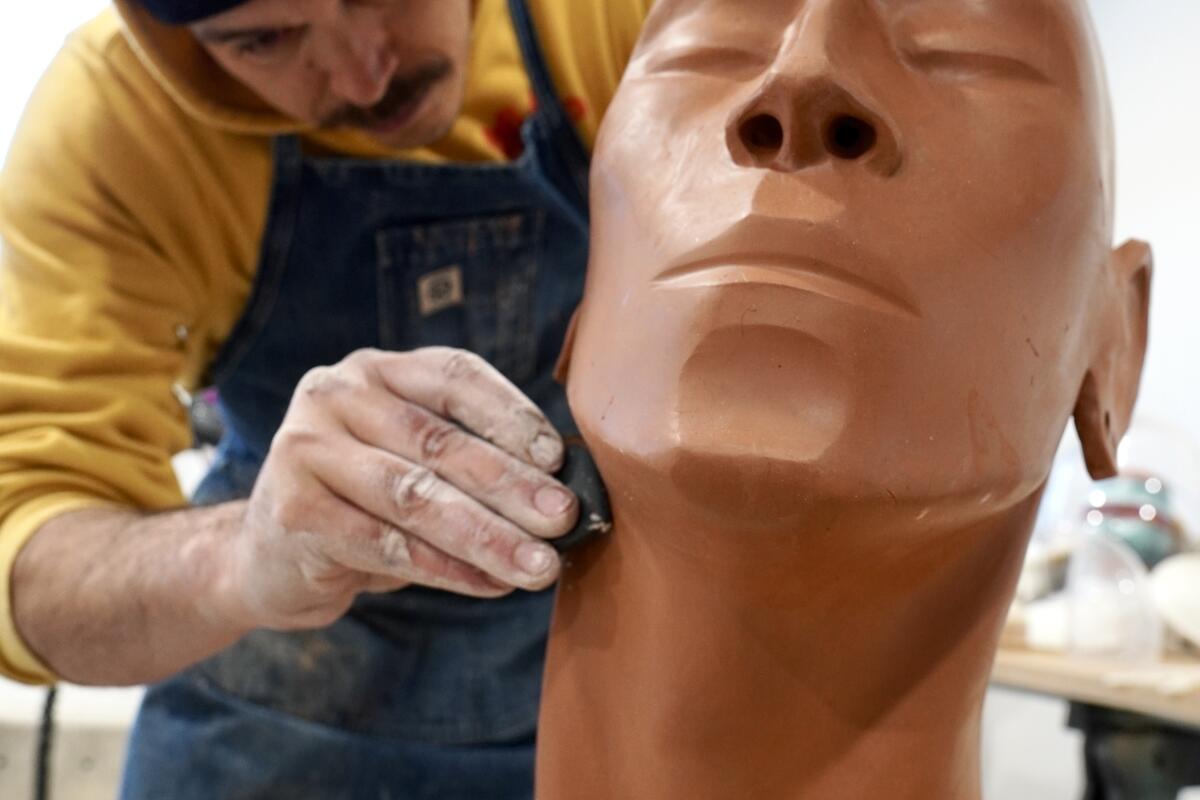 An artist sculpts the chiseled features of a clay-colored bust. 