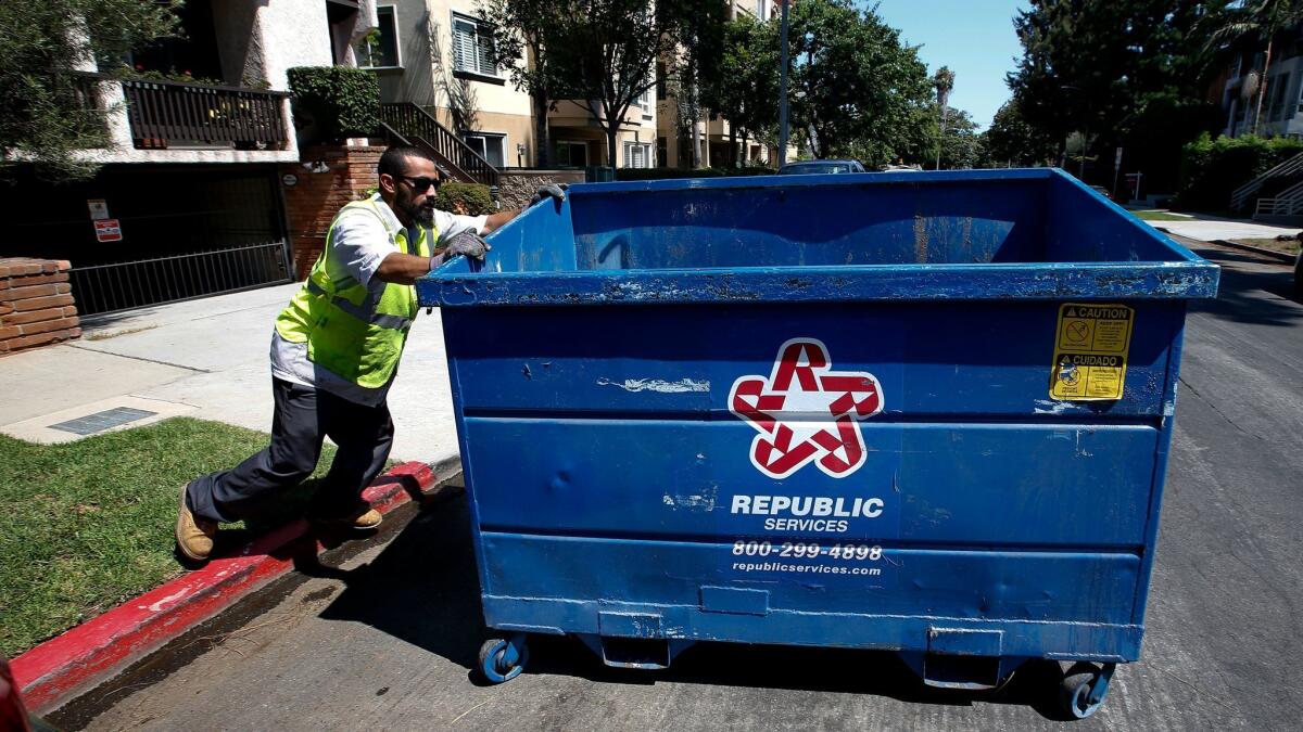 An employee with the trash hauler Athens Services moves a refuse bin outside a 14-unit condominium building in West Los Angeles.