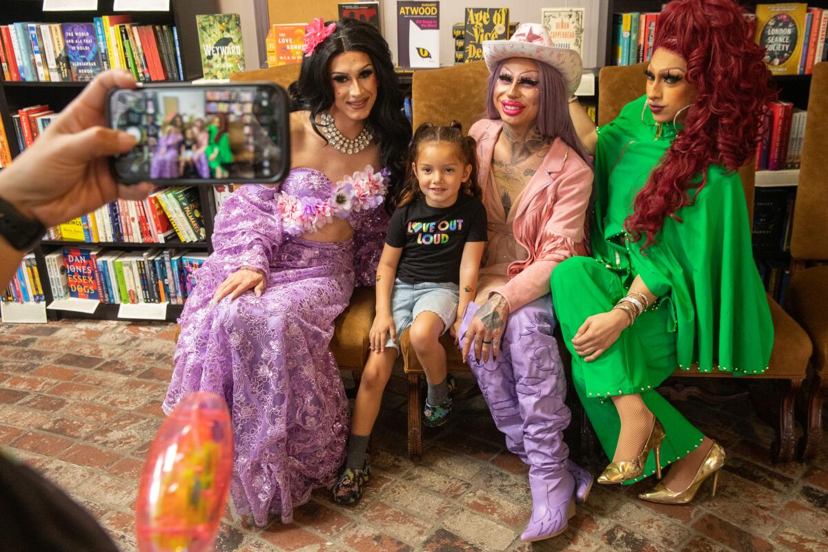A 4-year-old girl poses for a photo with three drag queens in a bookstore.