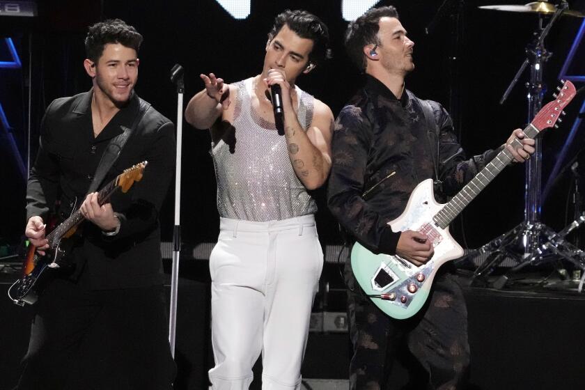 Three men on a stage, two of them holding up guitars