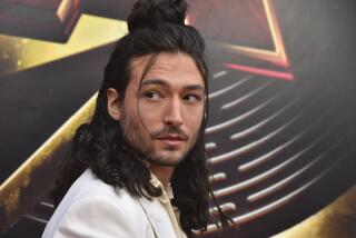 Ezra Miller looks over their shoulder while wearing a white blazer.