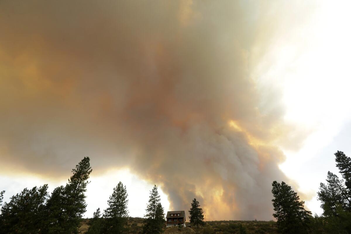 Smoke from an approaching wildfire looms over a home near Twisp, Wash., on Wednesday.