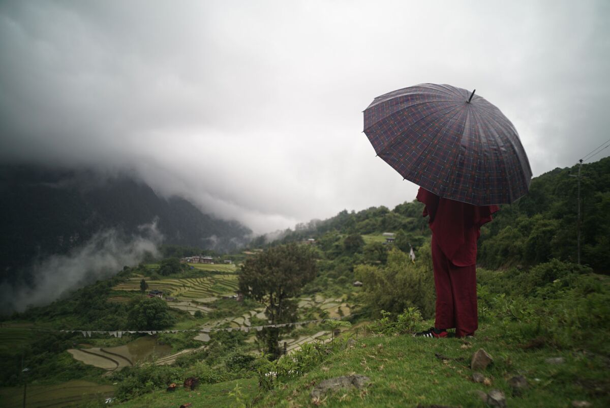A young monk with an umbrella overlooks his Himalayan village in the documentary "Sing Me a Song."
