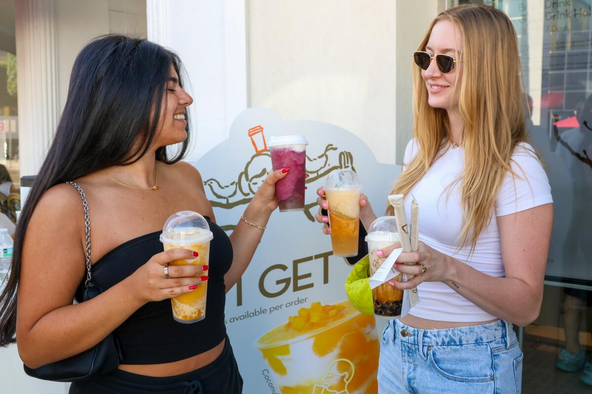 Two women each holding two drinks in plastic cups at Heytea