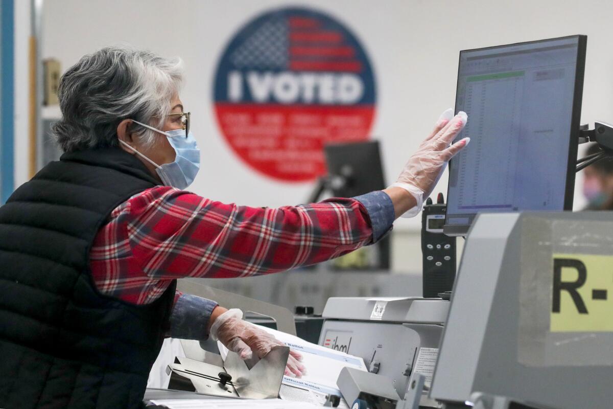 A woman touching a computer screen while processing ballots through machines, with a large "I voted" poster in the background