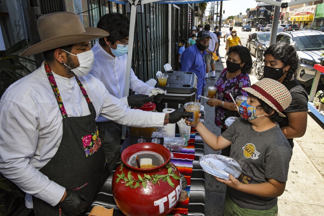 Two people hand out drinks to others outside