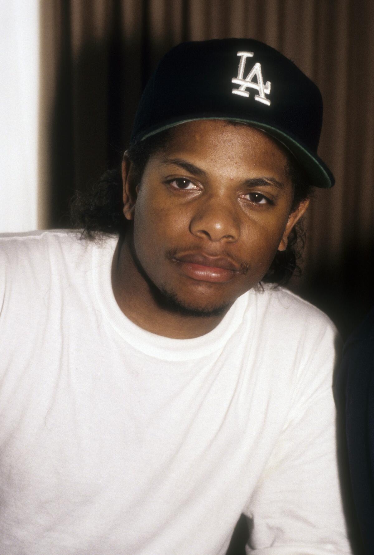 Eazy-E shows a serious face while clad in a white shirt and a baseball cap with the Dodgers' L.A. logo on the front