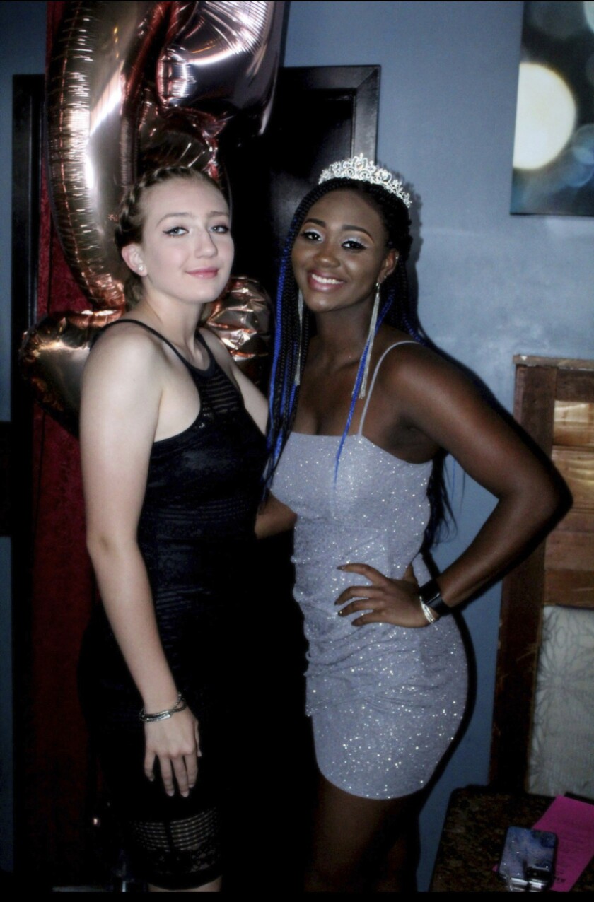 Two young women in party dresses pose for a photo.