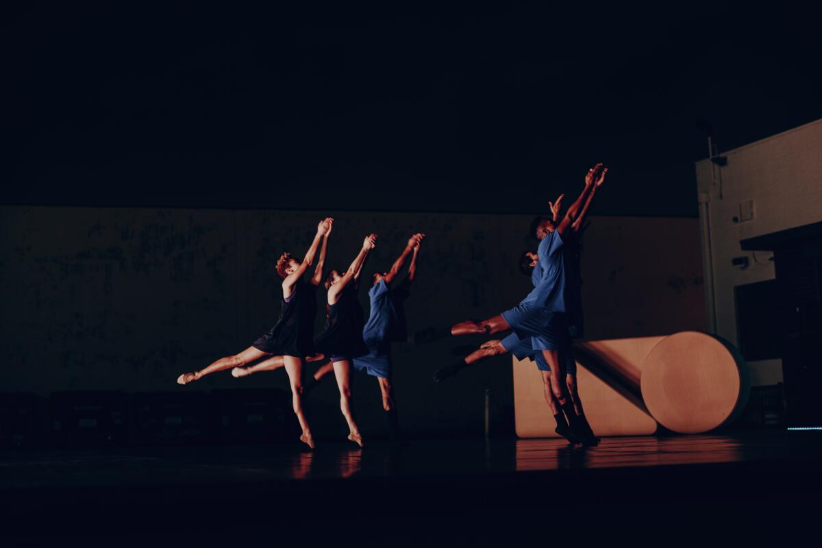 Dancers on a dimly-lit set perform before a backdrop of geometric shapes