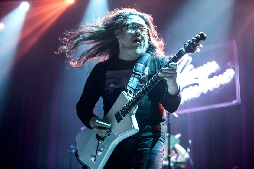 A man with long hair flying behind him plays an electric guitar on stage.