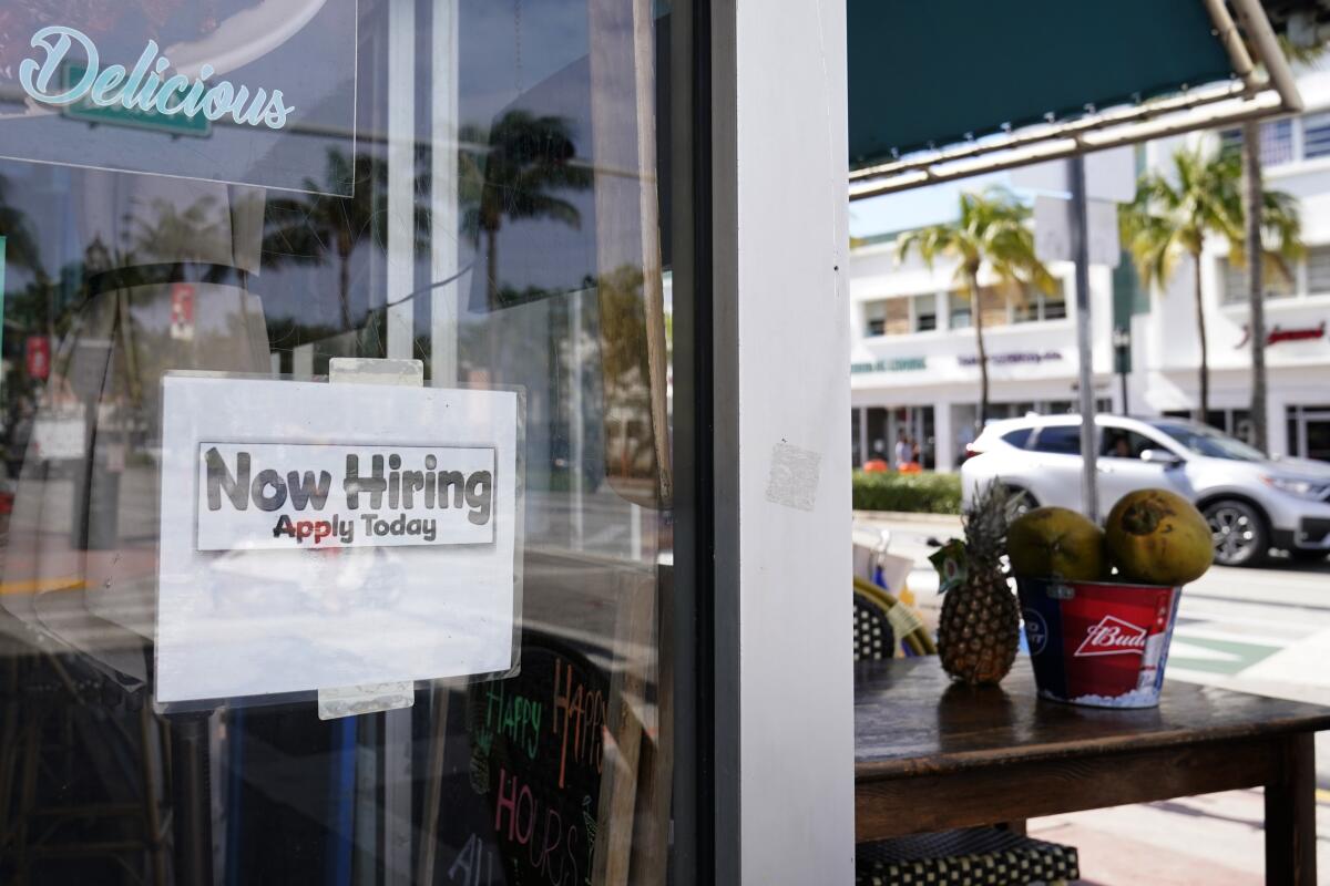 A "Now Hiring," sign is shown in the window of a restaurant