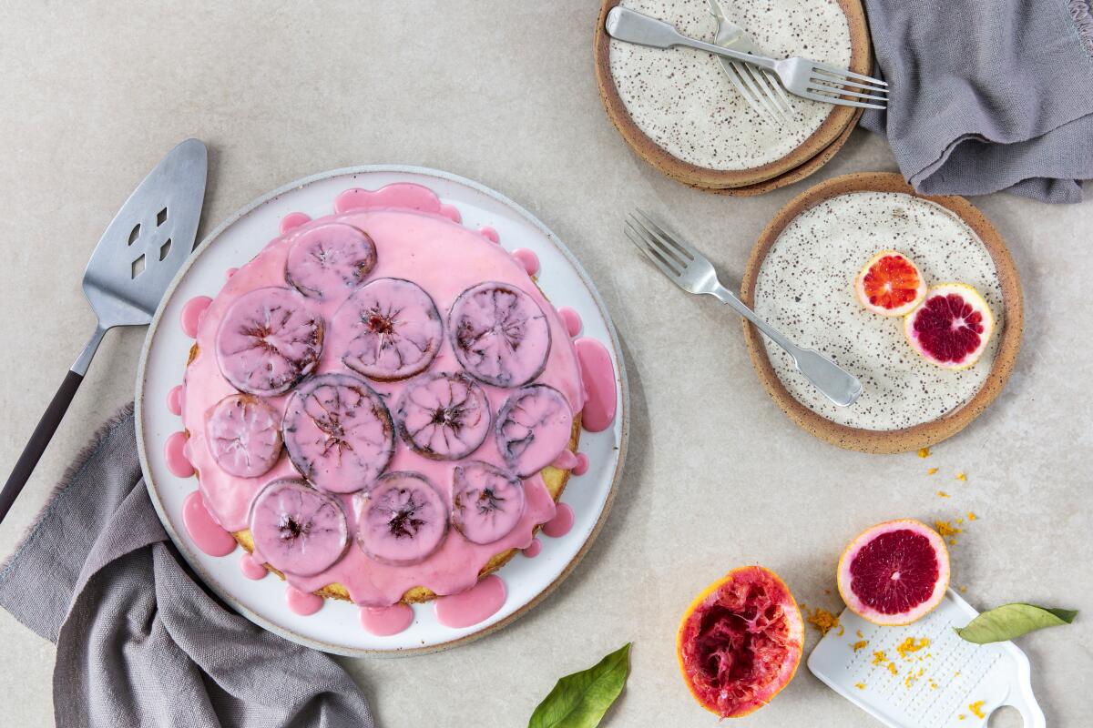 An overhead view of sliced citrus on a plate and a cake on a plate with pink frosting and citrus slices