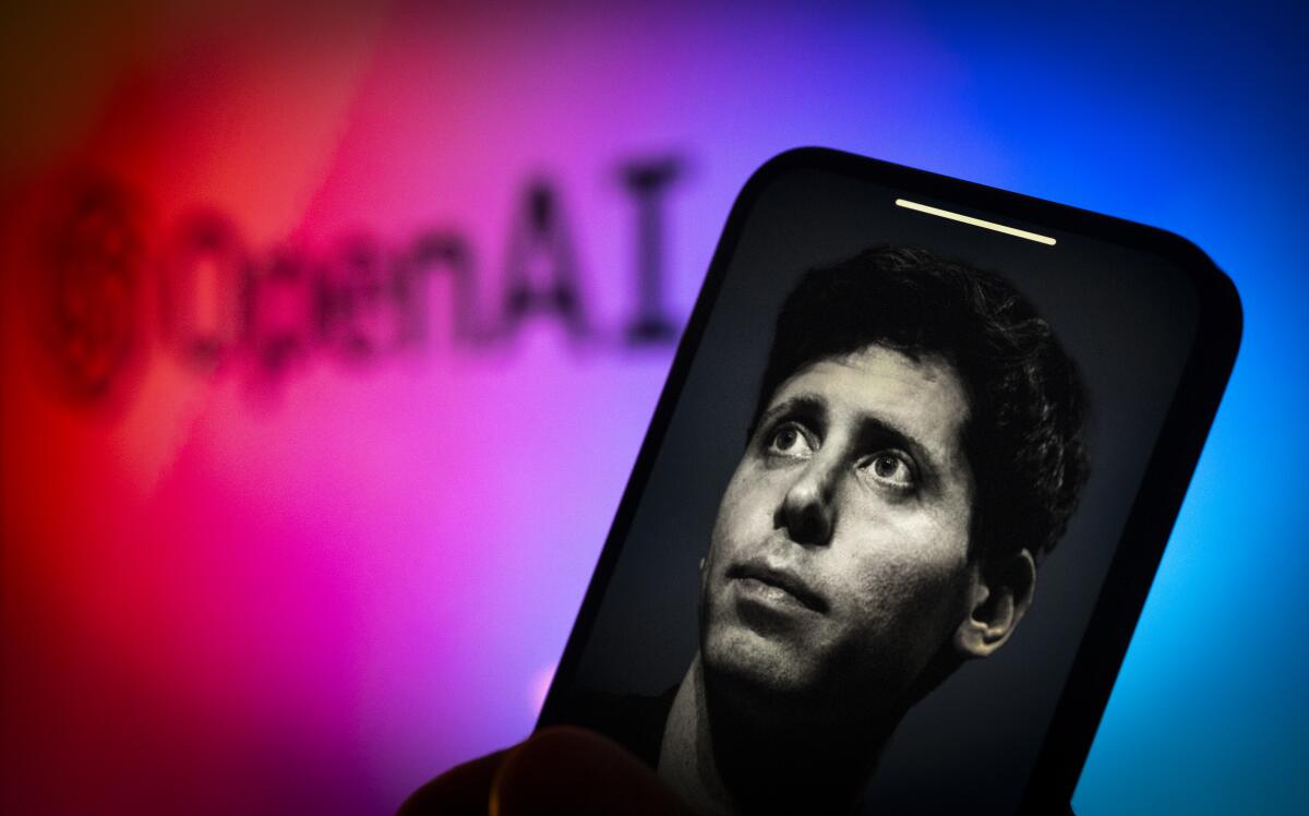 The face of Sam Altman is seen on a phone screen in front of an OpenAI sign