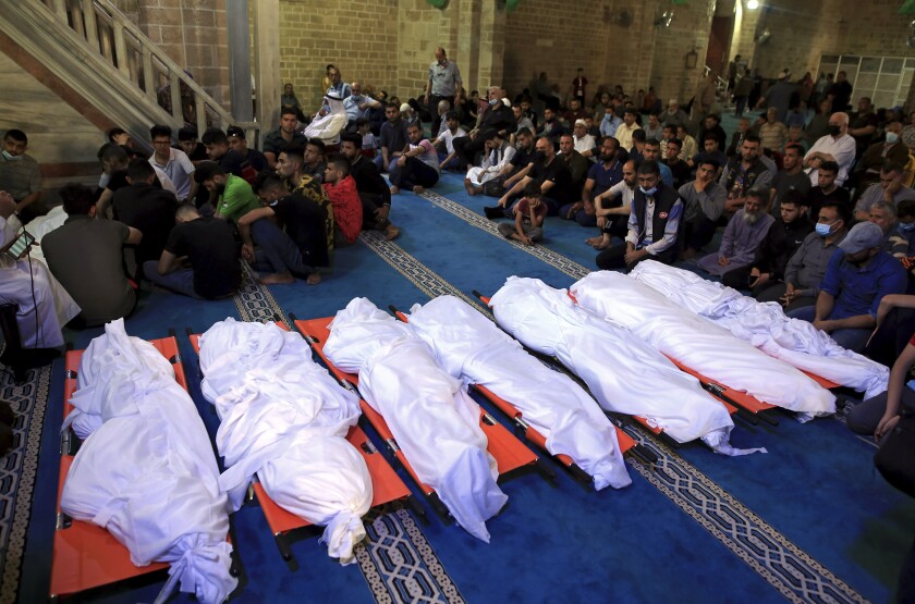 People kneel near bodies on stretchers that are wrapped in white.