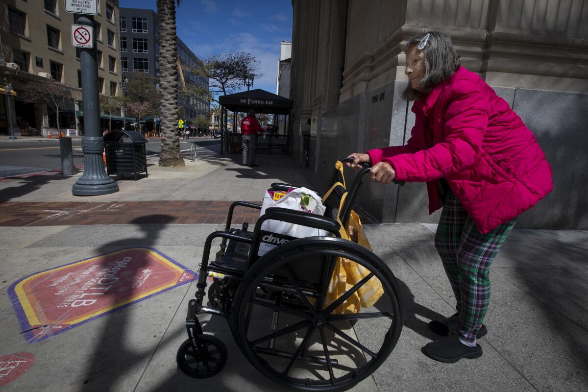 Rhonda Summerlin, 70, of Carson pushes her wheelchair down a Long Beach sidewalk on Sunday to pick up medicine and food. 