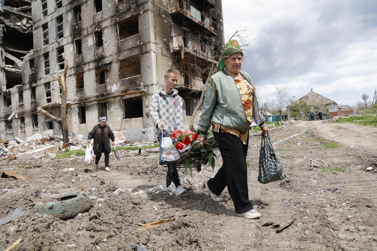 People carry bags past a multistory building that is scorched, with windows blown out