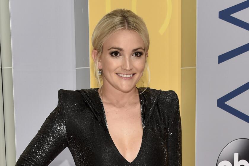 Jamie Lynn Spears in a black long sleeve dress with shoulder pads and a deep neckline, posing with her right hand on her hip