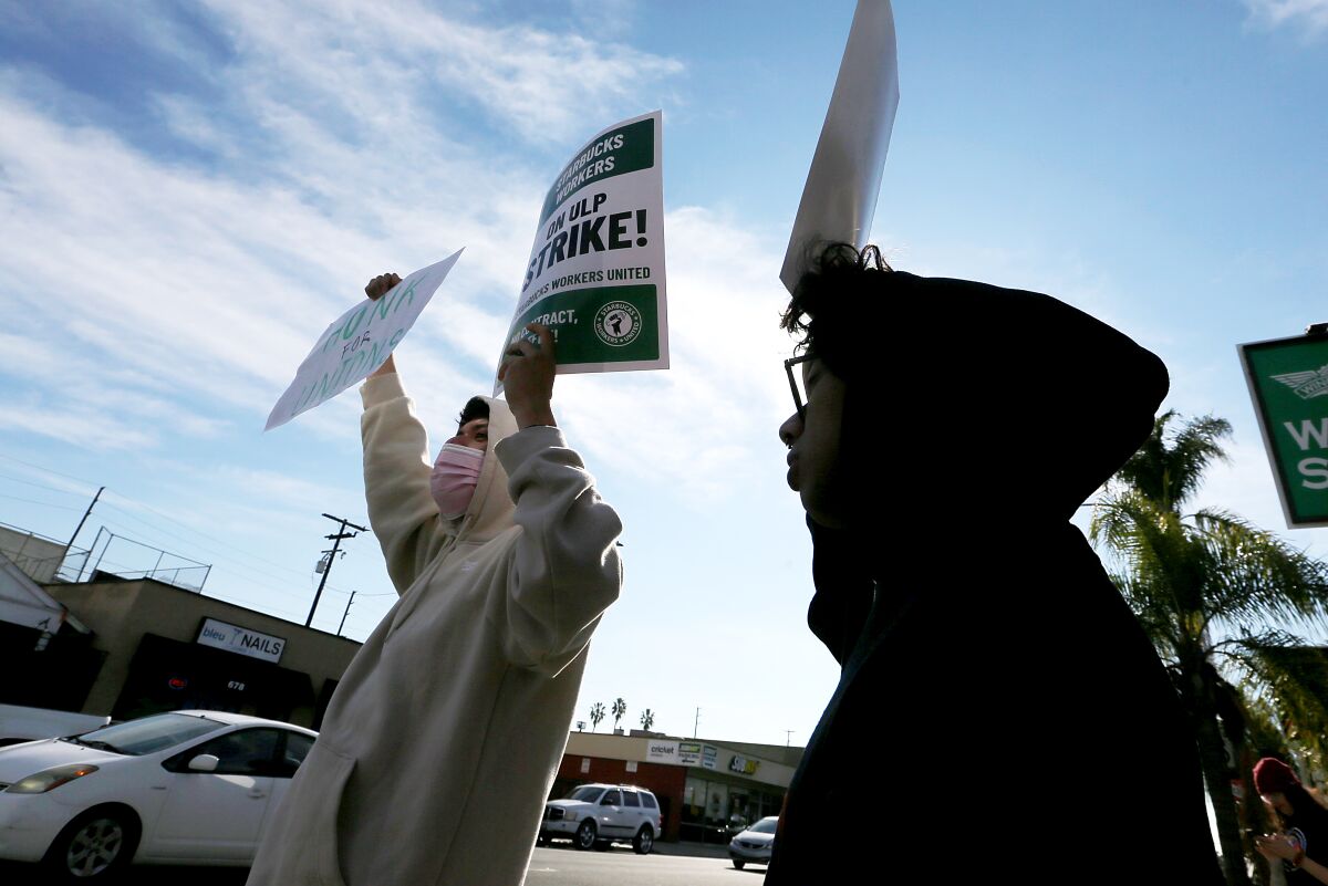 People in hoodies stand next to a city street holding up signs.