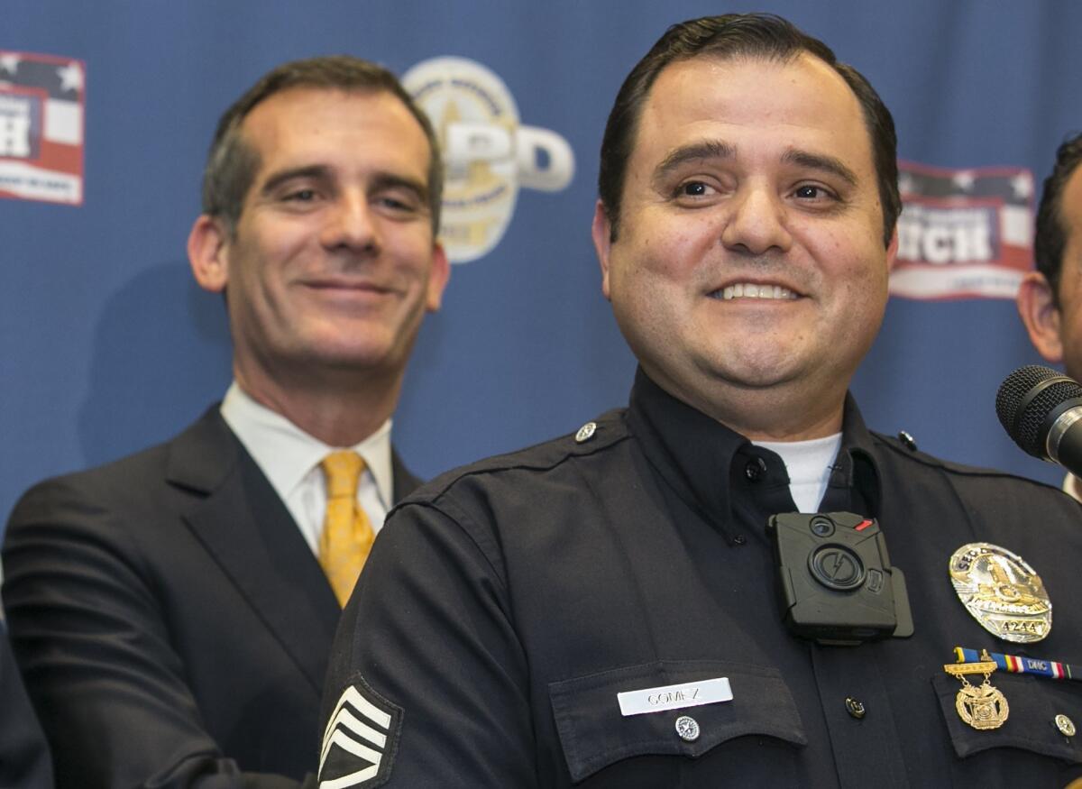 L.A. Police Sgt. Dan Gomez, right, wears an on-body video camera as he takes questions about the technology at a news conference. Mayor Eric Garcetti, left, announced a plan to equip 7,000 police officers with body cams by next summer.
