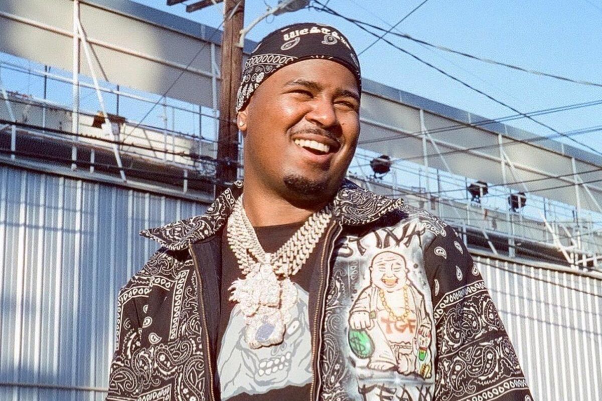 A smiling man wearing a jacket, chains and a bandanna.