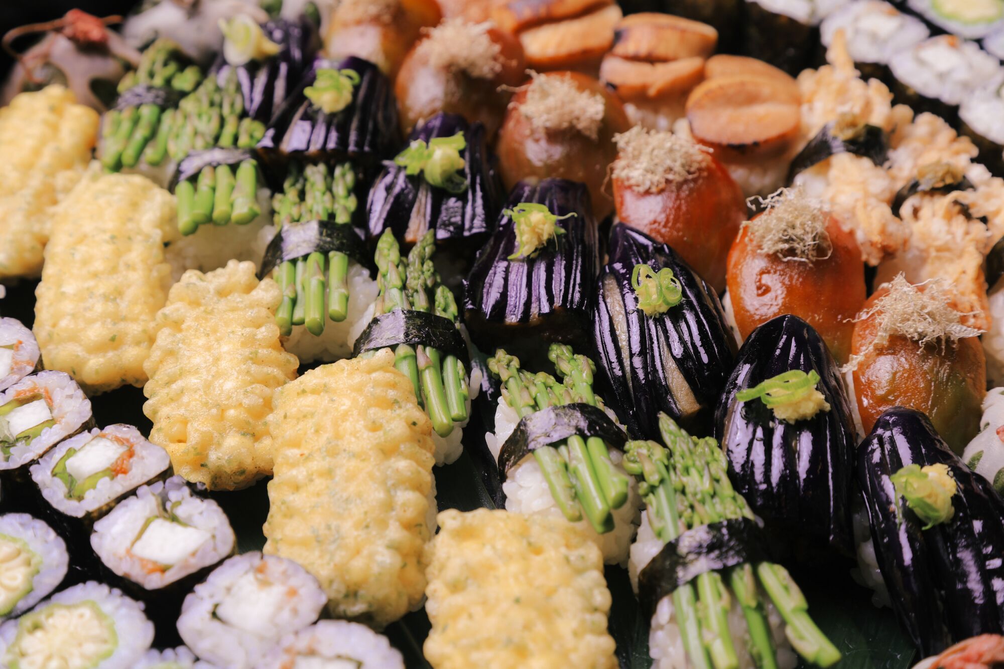 Rows of sushi topped with corn, eggplant, asparagus and other vegetables.