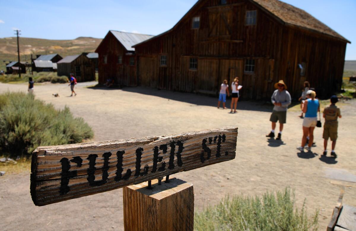 People walk among old wooden buildings. A wooden sign in the foreground says "Fuller St."